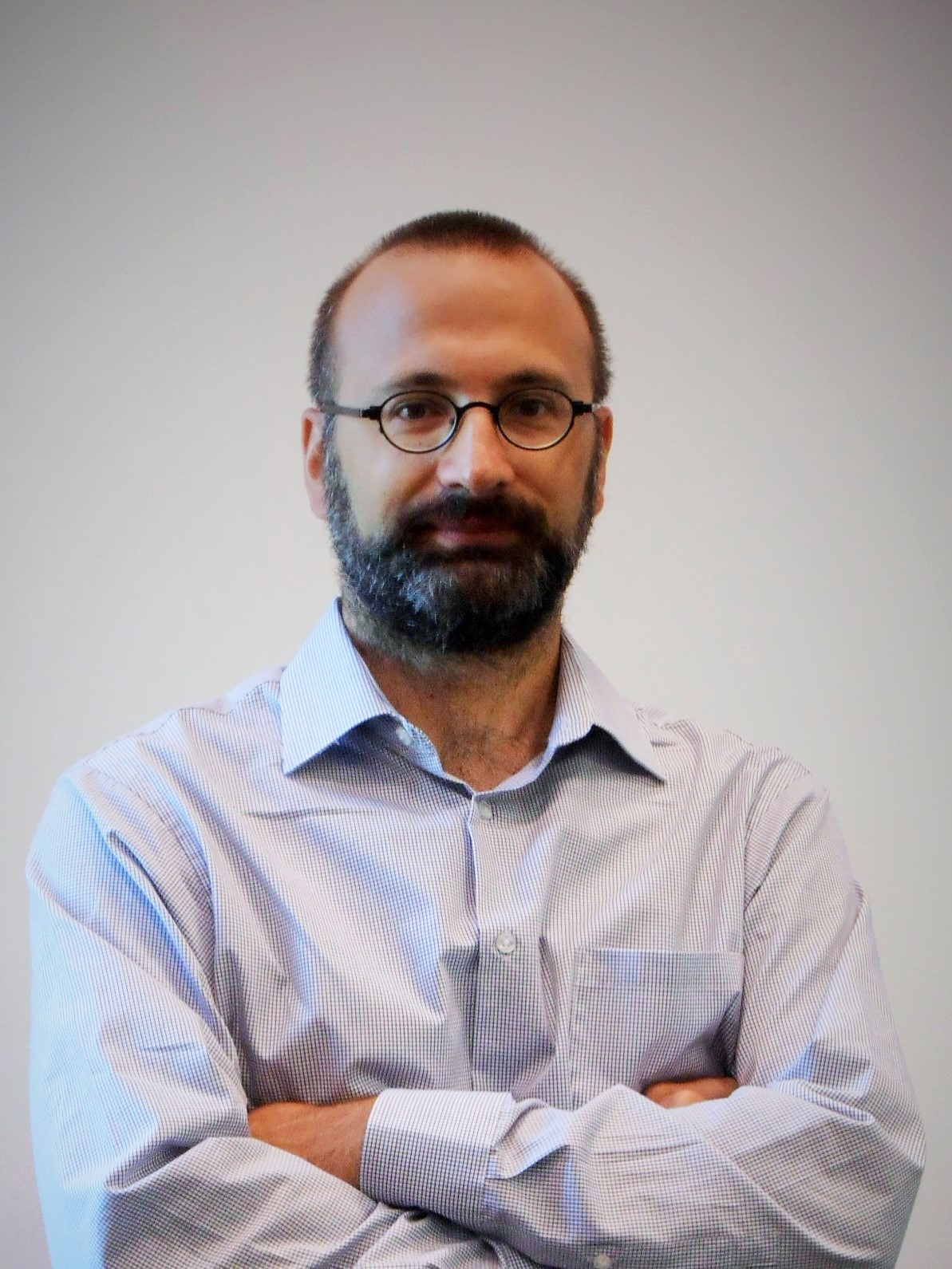 Colour headshot photo of Andrea Lanza wearing eye glasses, collar button down shirt, arms crossed.