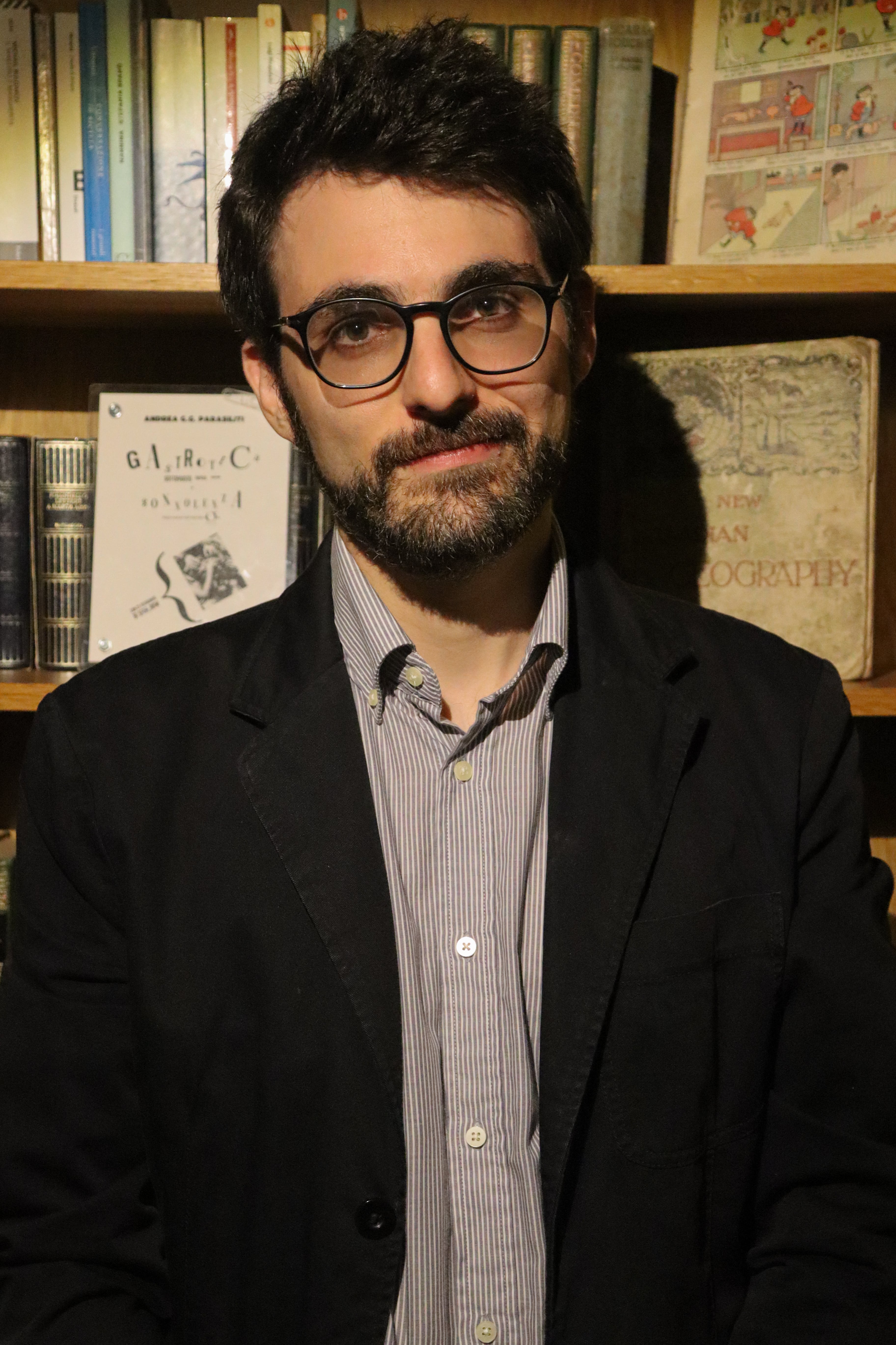 Colour medium shot photo of Alessio Aletta with bookshelves of books in background