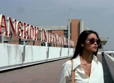 Colour image from the film of the protagonist, Emanuelle, in front of &amp;quot;Bangkok International Airport&amp;quot; signage, leaving the airport.