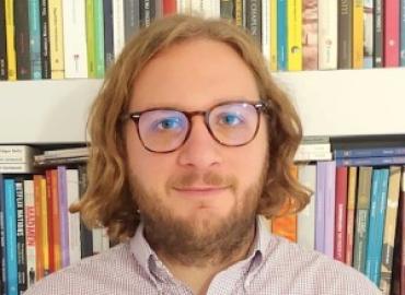 colour headshot photo of Damiano Garofalo wearing glasses and smiling, against shelves with books
