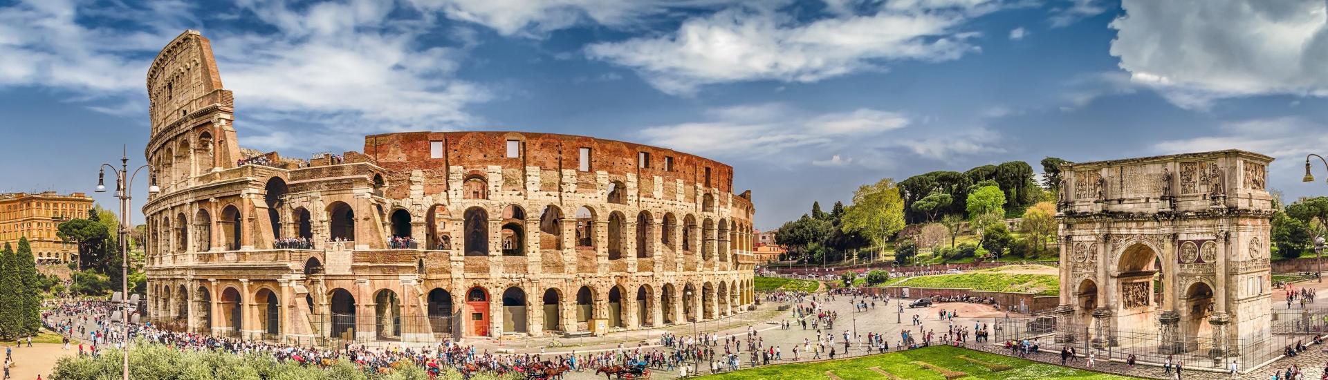 Panoramic colour stock photo of colosseum and arch in Rome with many people visiting monuments.